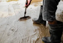 Osoba w gumowcach czyści szczotką zabłoconą, mokrą betonową posadzkę