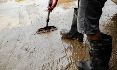 Osoba w gumowcach czyści szczotką zabłoconą, mokrą betonową posadzkę