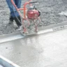 Robotnik prowadzi listwę wibracyjną po świeżo zalanej wylewce z mokrym połyskiem